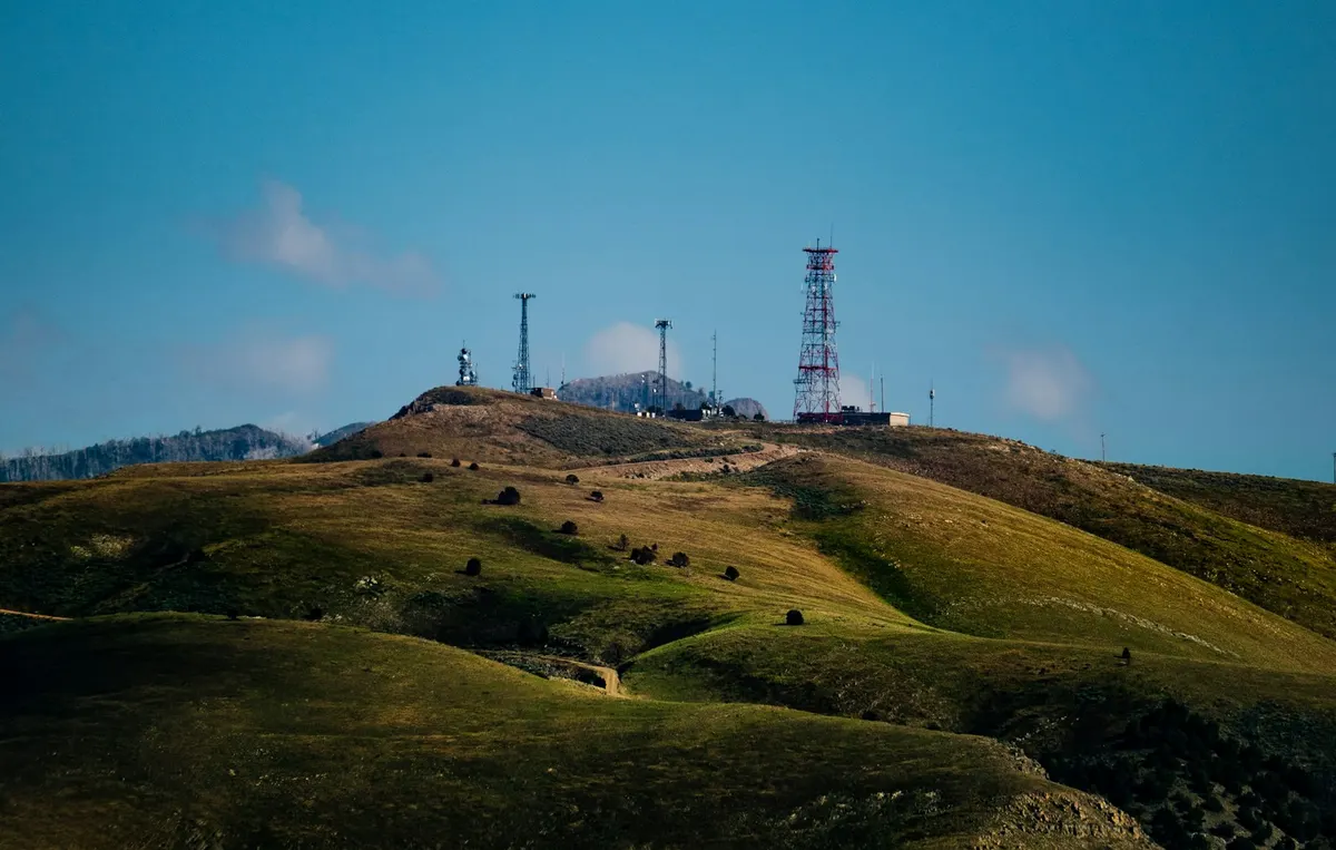Cell towers and communications equipment on a grassy hilltop.